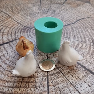 Könnte beinhalten: Eine türkisfarbene Silikonform zum Herstellen kleiner Keramik-Hühnerfiguren. Zwei weiße Keramikhühner und eine Euro-Münze sind ebenfalls abgebildet.