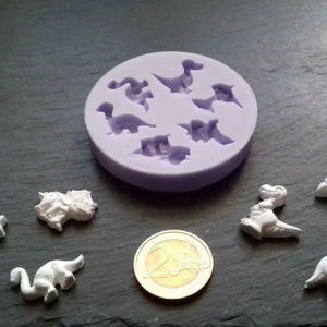 Könnte beinhalten: Eine lila Silikonform mit acht Dinosaurierformen. Die Form befindet sich auf einer grauen Oberfläche mit mehreren weißen Dinosaurierfiguren.
