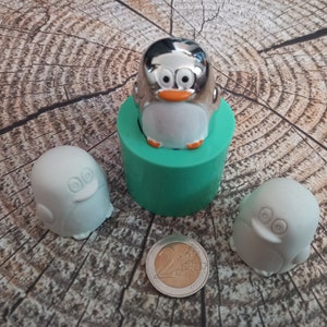 Könnte beinhalten: Drei pinguinförmige Silikonformen, zwei sind weiß und eine ist silber. Die silberne Form befindet sich in einer grünen Silikonformbasis.