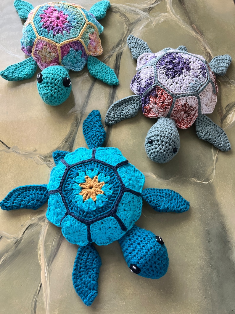 May include: Three crocheted sea turtle toys with colorful shells. The turtles are made with different colored yarn, including blue, green, purple, and pink.