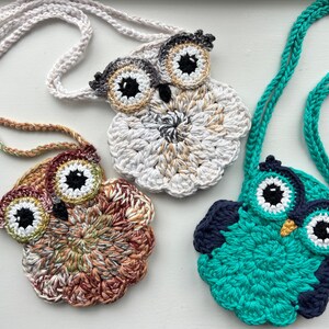 May include: Three crocheted owl purses with different colored yarn. The owls have black eyes and beaks. The purses are attached to crocheted cords.