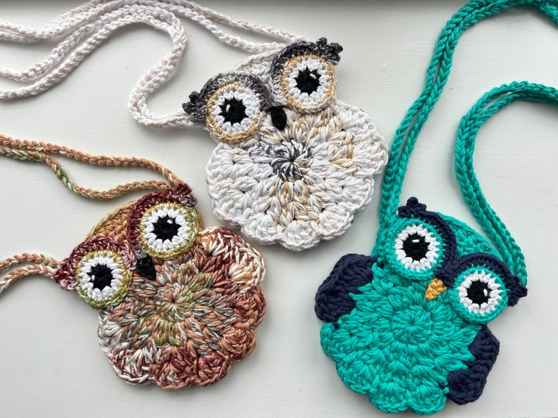 May include: Three crocheted owl purses with different colored yarn. The owls have black eyes and beaks. The purses are attached to crocheted cords.