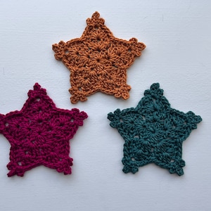 May include: Three crocheted star-shaped coasters in different colors: burgundy, mustard yellow, and teal.