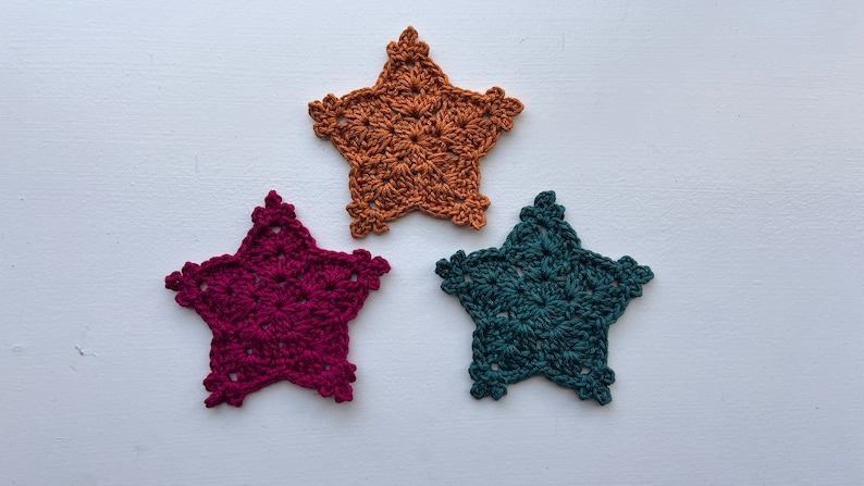 May include: Three crocheted star-shaped coasters in different colors: burgundy, mustard yellow, and teal.