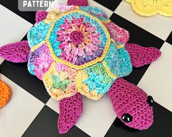 Puede incluir: Un juguete de tortuga tejido a ganchillo con un caparazón multicolor hecho de motivos florales unidos en tonos rosa, azul y amarillo. La cabeza y las aletas son de hilo magenta sólido con ojos de seguridad negros. El texto dice CROCHET PATTERN.