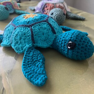 May include: Three crocheted sea turtle toys. The largest turtle is teal blue with black accents and yellow details. The two smaller turtles are multi-colored.
