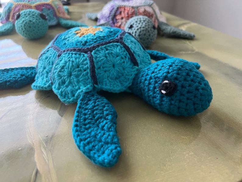 May include: Three crocheted sea turtle toys. The largest turtle is teal blue with black accents and yellow details. The two smaller turtles are multi-colored.