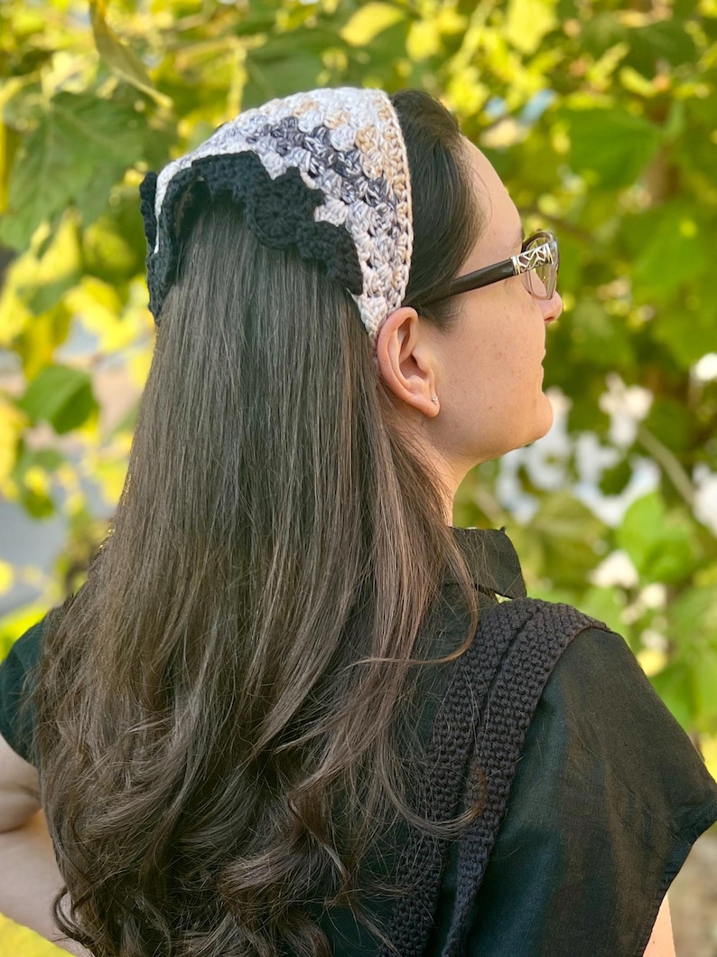 May include: A woman with long brown hair wearing a black crocheted headband with a white and gray pattern. The headband has a scalloped edge.
