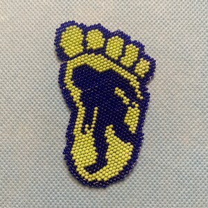 May include: A beaded foot-shaped design. The outline and border are made of dark blue beads, while the interior is filled with light yellow beads. The design is on a light blue background.
