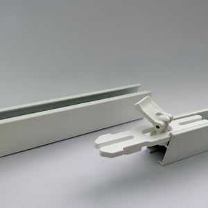 Pode incluir: Uma imagem de perto de componentes de trilhos de cortina brancos. A imagem mostra dois trilhos de metal brancos e um conector de plástico branco. O conector está parcialmente engatado, mostrando como os trilhos se juntam. O fundo é cinza claro liso.