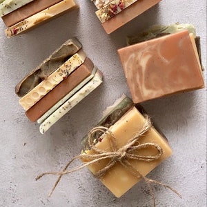 Könnte beinhalten: Ein Stapel handgemachter Seifenstücke mit verschiedenen Farben und Mustern, darunter Braun, Beige und Grün. Die Seifenstücke sind in einem Stapel angeordnet und mit Schnur gebunden.