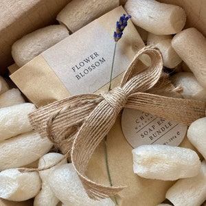 May include: A brown paper package with a natural twine bow and a label that says "Flower Blossom". The package is surrounded by white packing peanuts and a smaller label that says "CHLOE Naturals SOAP  EN BUNDLE  wt. 180g".