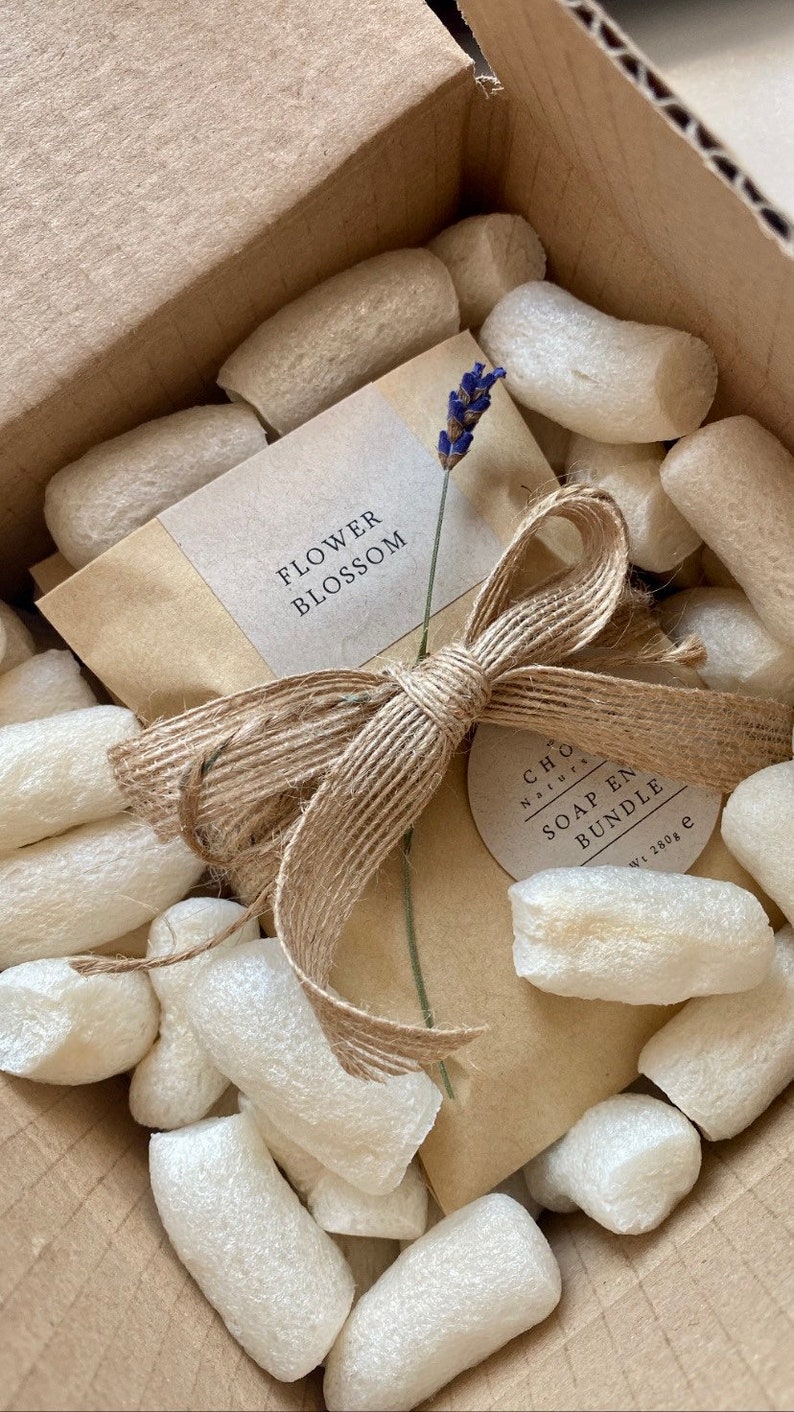 May include: A brown paper package with a natural twine bow and a label that says "Flower Blossom". The package is surrounded by white packing peanuts and a smaller label that says "CHLOE Naturals SOAP  EN BUNDLE  wt. 180g".