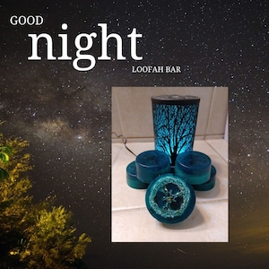 Può includere: Una pila di saponette di luffa verde turchese con un diffusore a forma di albero blu e nero sullo sfondo. Il testo "GOOD night LOOFAH BAR" è visibile nell'immagine.
