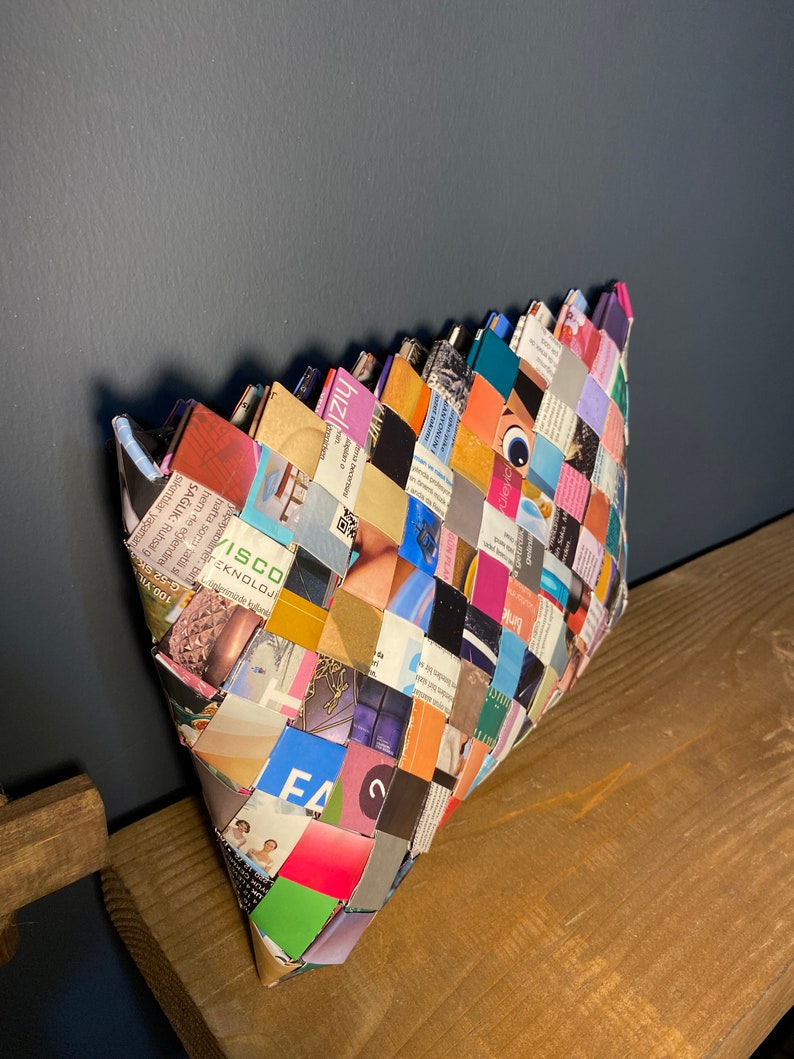 May include: A woven clutch bag made from recycled magazine pages. The bag is a patchwork of colorful magazine clippings and has a unique, geometric design.