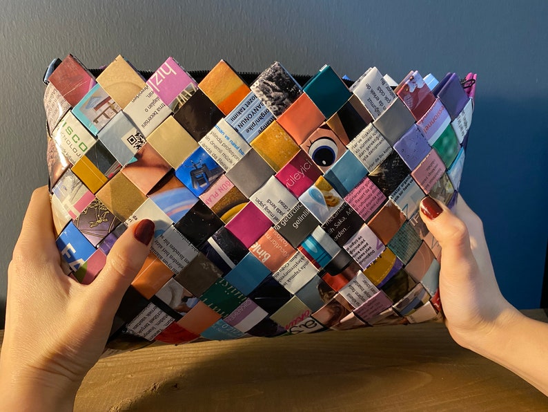 May include: A colorful woven clutch bag made from recycled magazine pages. The bag is woven in a diamond pattern and features a variety of colors and patterns.