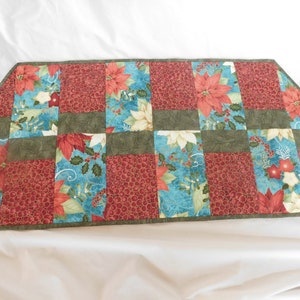 May include: A green, red, and blue quilted table runner with a Christmas poinsettia pattern. The runner is made of fabric squares sewn together.