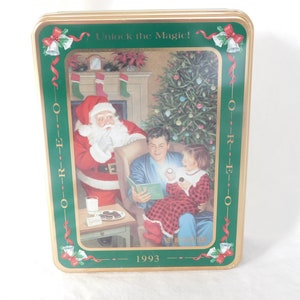 May include: A green and gold Christmas tin with a picture of Santa Claus, a man, and a child. The tin has the words "Unlock the Magic!" and "OREO" on it. The year 1993 is printed on the bottom.