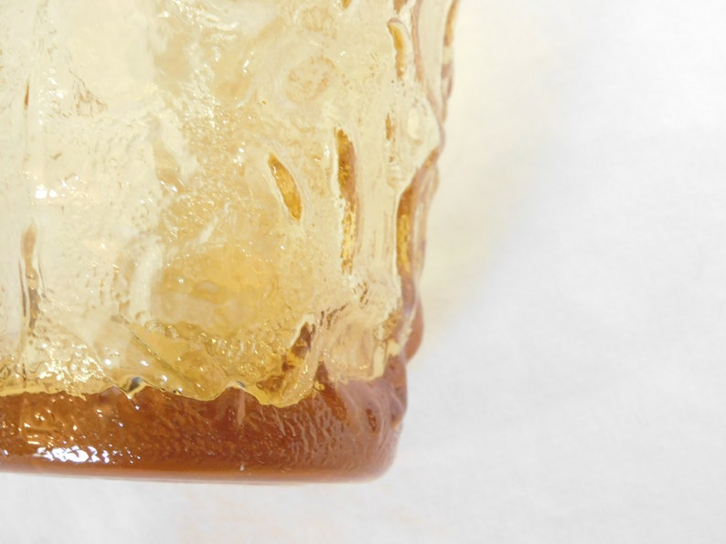 May include: A close-up of a clear glass vase with a textured surface. The vase is amber in color and has a rounded bottom.