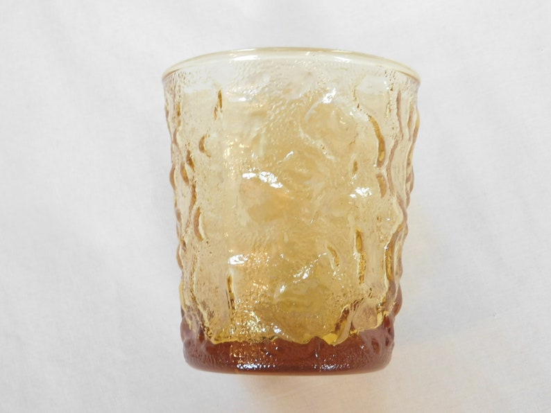 May include: A clear amber glass tumbler with a textured, raised design. The glass has a rounded bottom and a slightly flared top.