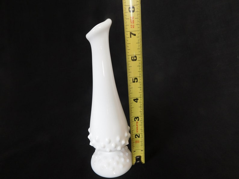 May include: White milk glass bud vase with a textured, dotted design. The vase is approximately 15 cm tall.