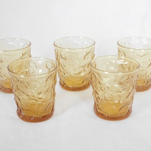 May include: Set of five amber glass tumblers with a textured, embossed design. The glasses are clear and have a slightly frosted appearance.