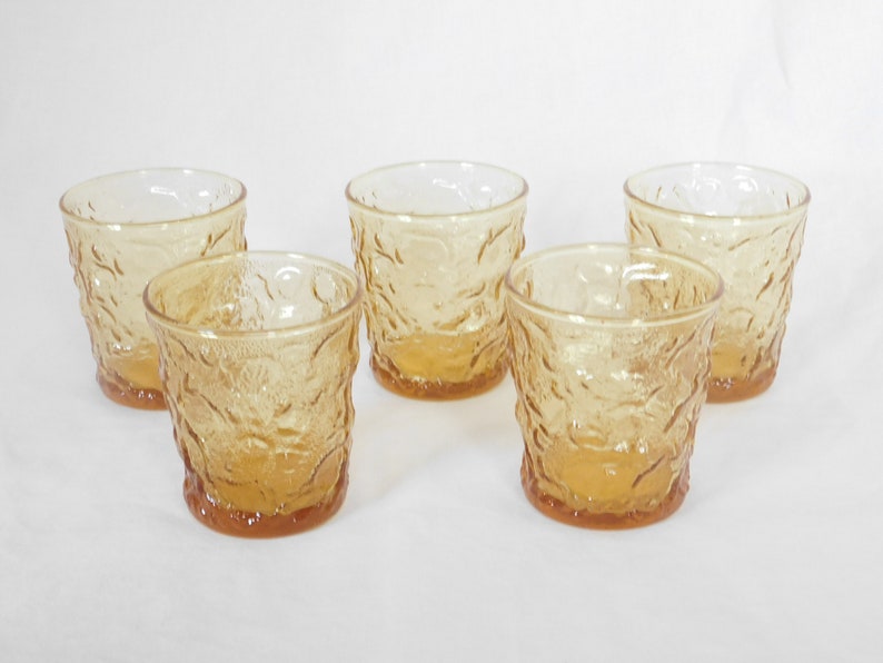 May include: Set of five amber glass tumblers with a textured, embossed design. The glasses are clear and have a slightly frosted appearance.