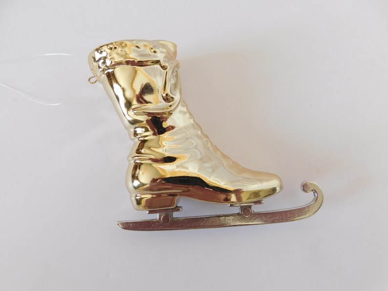 Puede incluir: Adorno de pat&iacute;n de hielo de color dorado con una cuchilla plateada. El pat&iacute;n est&aacute; dise&ntilde;ado para parecerse a un pat&iacute;n de hielo tradicional con una bota y una cuchilla.