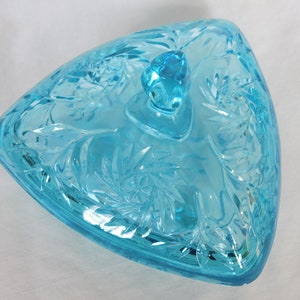 May include: A triangular glass candy dish with a lid. The dish is made of clear blue glass with a cut glass design. The lid has a knob on top.