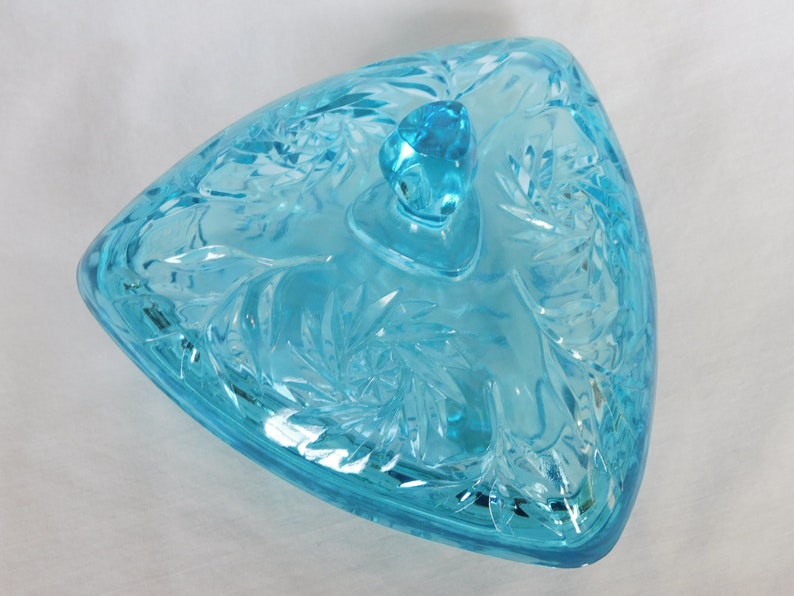 May include: A triangular glass candy dish with a lid. The dish is made of clear blue glass with a cut glass design. The lid has a knob on top.
