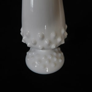 May include: White milk glass vase with a textured, bumpy surface. The vase has a wide base and a narrow neck.