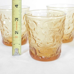 May include: Set of four amber glass tumblers with a textured, raised design. The tumblers are approximately 3 inches tall.