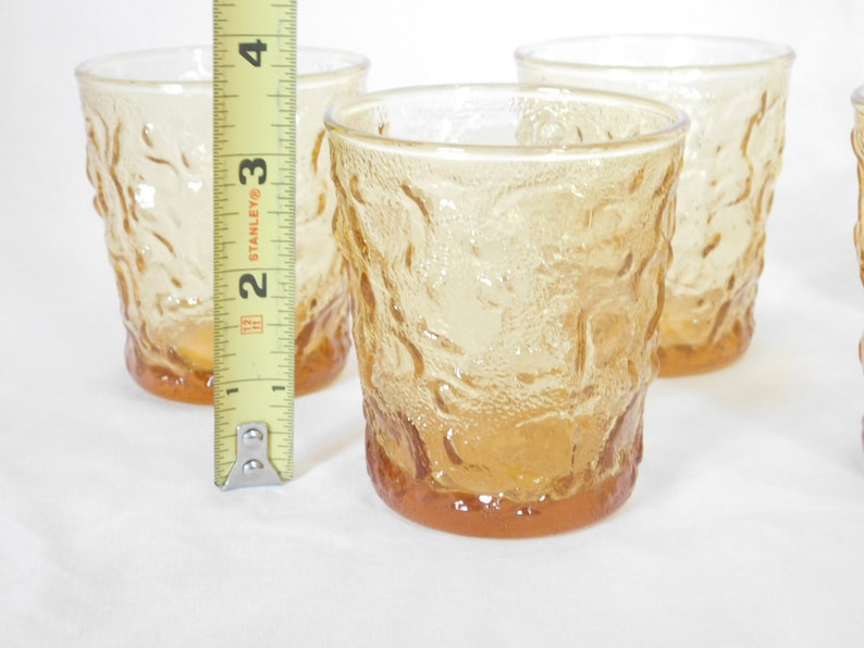 May include: Set of four amber glass tumblers with a textured, raised design. The tumblers are approximately 3 inches tall.