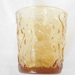 May include: A clear amber glass tumbler with a textured, raised pattern. The glass has a rounded bottom and a straight, slightly flared top.