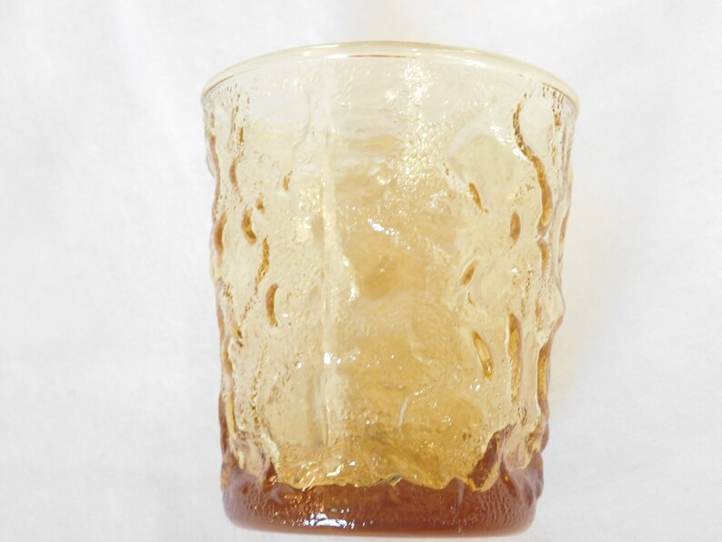 May include: A clear amber glass tumbler with a textured, raised pattern. The glass has a rounded bottom and a straight, slightly flared top.