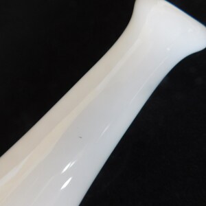 May include: A white ceramic vase with a smooth, rounded shape. The vase is tall and slender, with a narrow opening at the top.