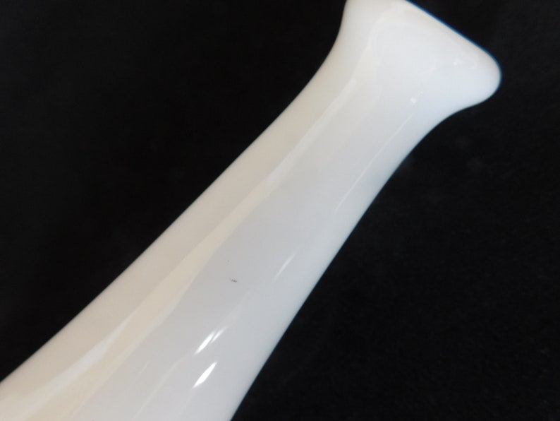 May include: A white ceramic vase with a smooth, rounded shape. The vase is tall and slender, with a narrow opening at the top.