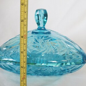 May include: A blue glass candy dish with a lid. The dish is oval shaped and has a swirl pattern. The lid has a knob on top.