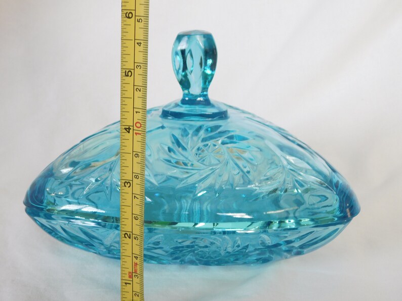 May include: A blue glass candy dish with a lid. The dish is oval shaped and has a swirl pattern. The lid has a knob on top.