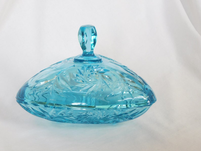 May include: A blue glass candy dish with a lid and a swirl design. The dish is shaped like a heart and has a handle on the lid.