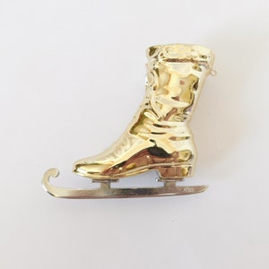 Puede incluir: Adorno de pat&iacute;n de hielo de color dorado con un dise&ntilde;o de bota detallado y una cuchilla de metal plateado.