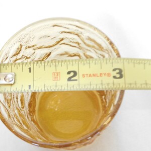 May include: A clear amber glass cup with a textured surface. The cup is 2 inches in diameter.