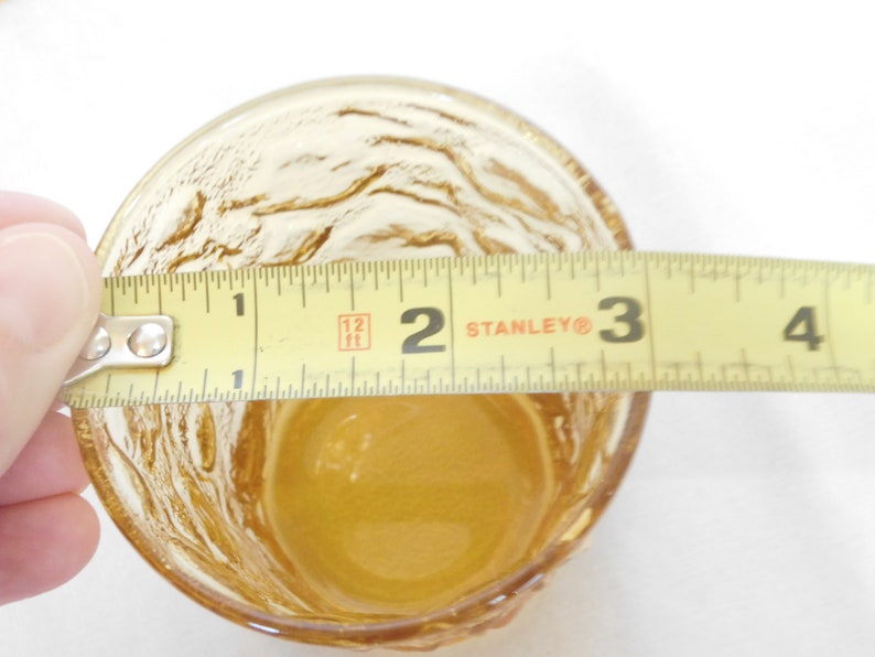 May include: A clear amber glass cup with a textured surface. The cup is 2 inches in diameter.