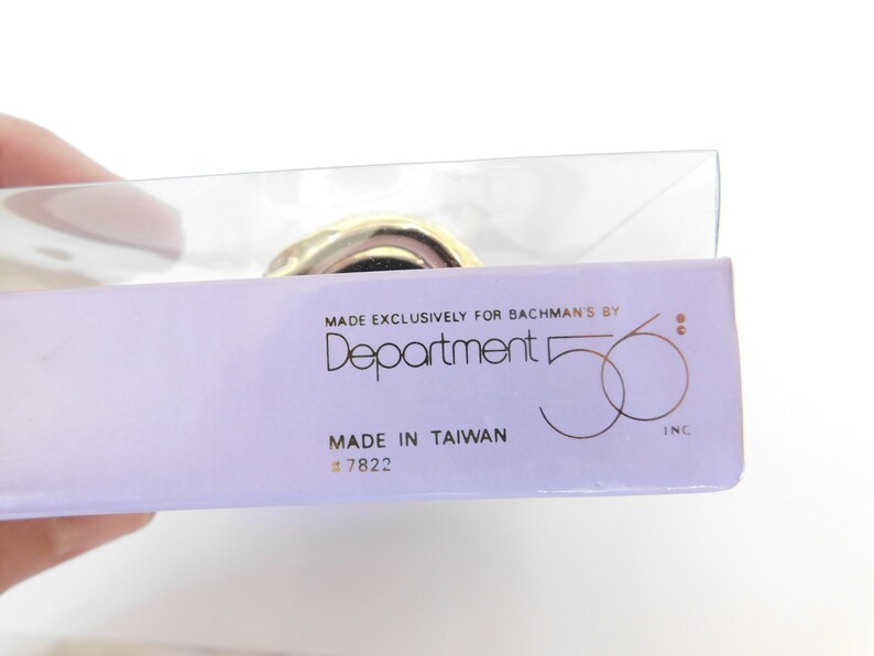 Puede incluir: Primer plano de una etiqueta de producto p&uacute;rpura y blanca con el texto "Made Exclusively for Bachman's by Department 56 Inc." y "Made in Taiwan # 7822".
