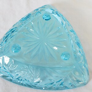 May include: A light blue glass bowl with a starburst pattern and three feet. The bowl is triangular in shape.