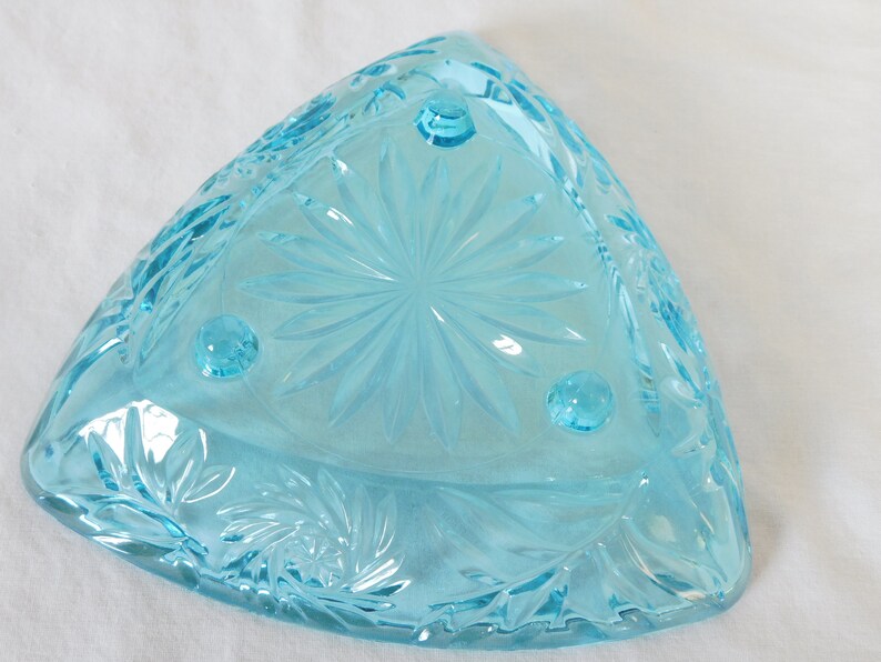May include: A light blue glass bowl with a starburst pattern and three feet. The bowl is triangular in shape.