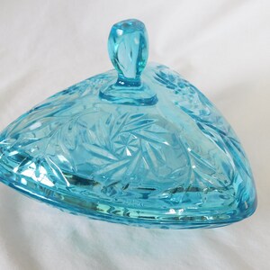 May include: A triangular glass candy dish with a lid. The dish is made of clear blue glass with a cut glass pattern. The lid has a knob on top.