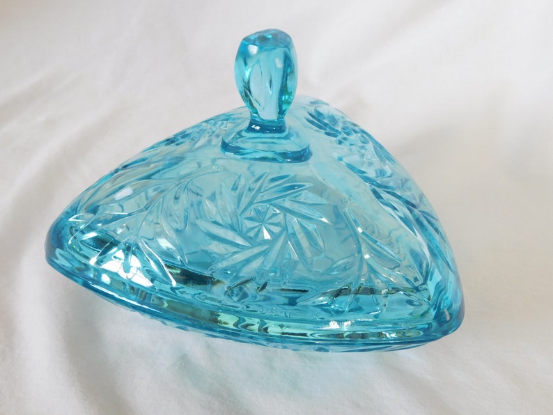 May include: A triangular glass candy dish with a lid. The dish is made of clear blue glass with a cut glass pattern. The lid has a knob on top.
