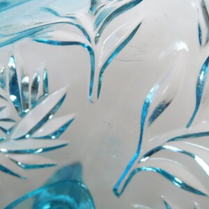May include: Close-up of a blue glass bowl with a cut glass design. The bowl has a delicate, intricate pattern of leaves and swirls.