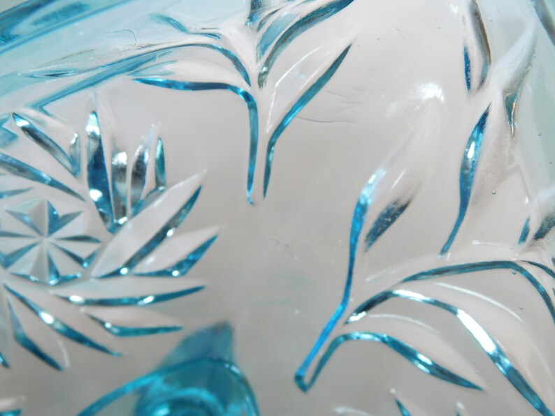 May include: Close-up of a blue glass bowl with a cut glass design. The bowl has a delicate, intricate pattern of leaves and swirls.